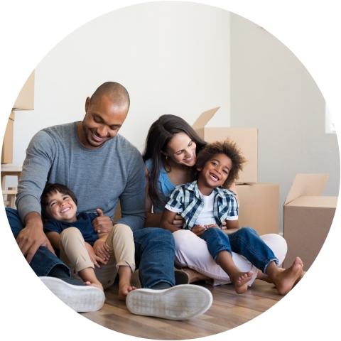 Family sitting on the floor of a home with boxes around them