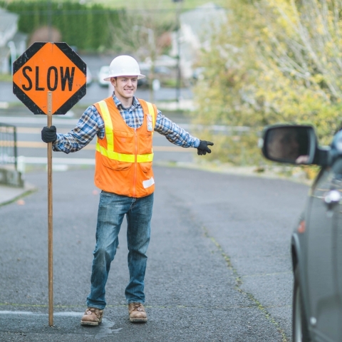 Flagger in an orange safety vest and helmet directing traffic