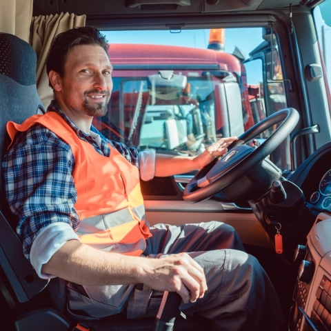 A man in a yellow safety vest sitting in the cab of a semi truck