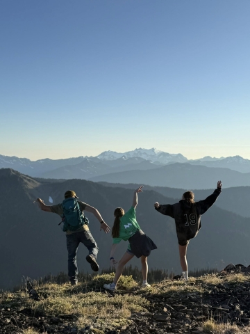 three people with their backs to the camera striking funny poses in front of a mountain range