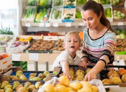 Mom and son in the produce department happily choosing a mango from a bin