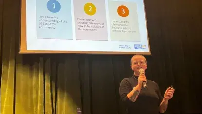 A person with a shaved head giving a presentation while standing in front of a projected image