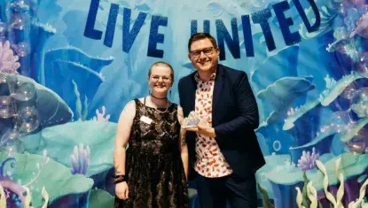 Two people standing in front of an under the sea backdrop. One person holds an award. 