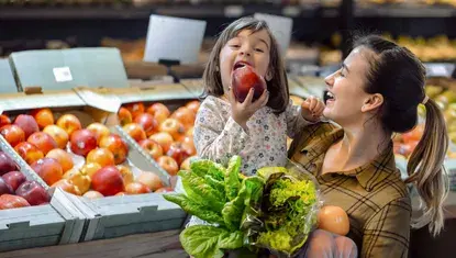 Woman holding young girl who is eating an apple