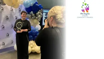 Person smiling, holding an award, and having their photo taken